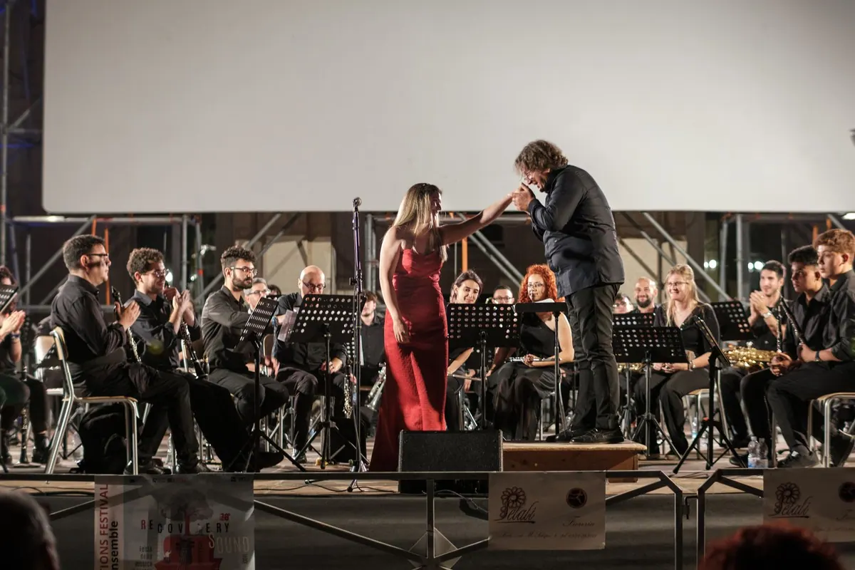 A soloist in a red dress and the conductor in front of the orchestra