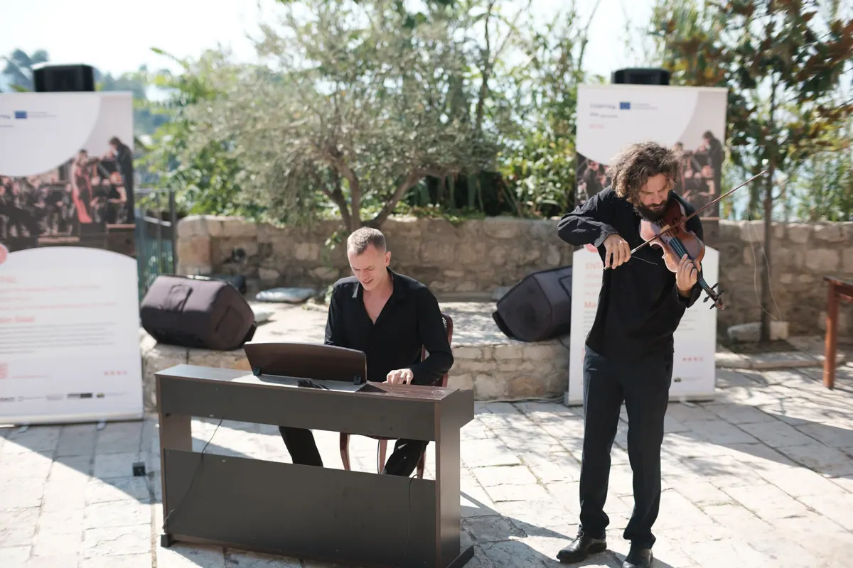 A pianist and a violinist playing on a stone terrace between the project banners