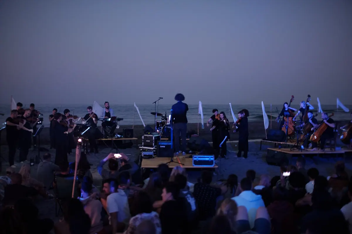Crnogorski orkestar mladih na bini na Velikoj plaži u sumrak, publika sjedi na pijesku, Festival mladih umjetnika 2025.