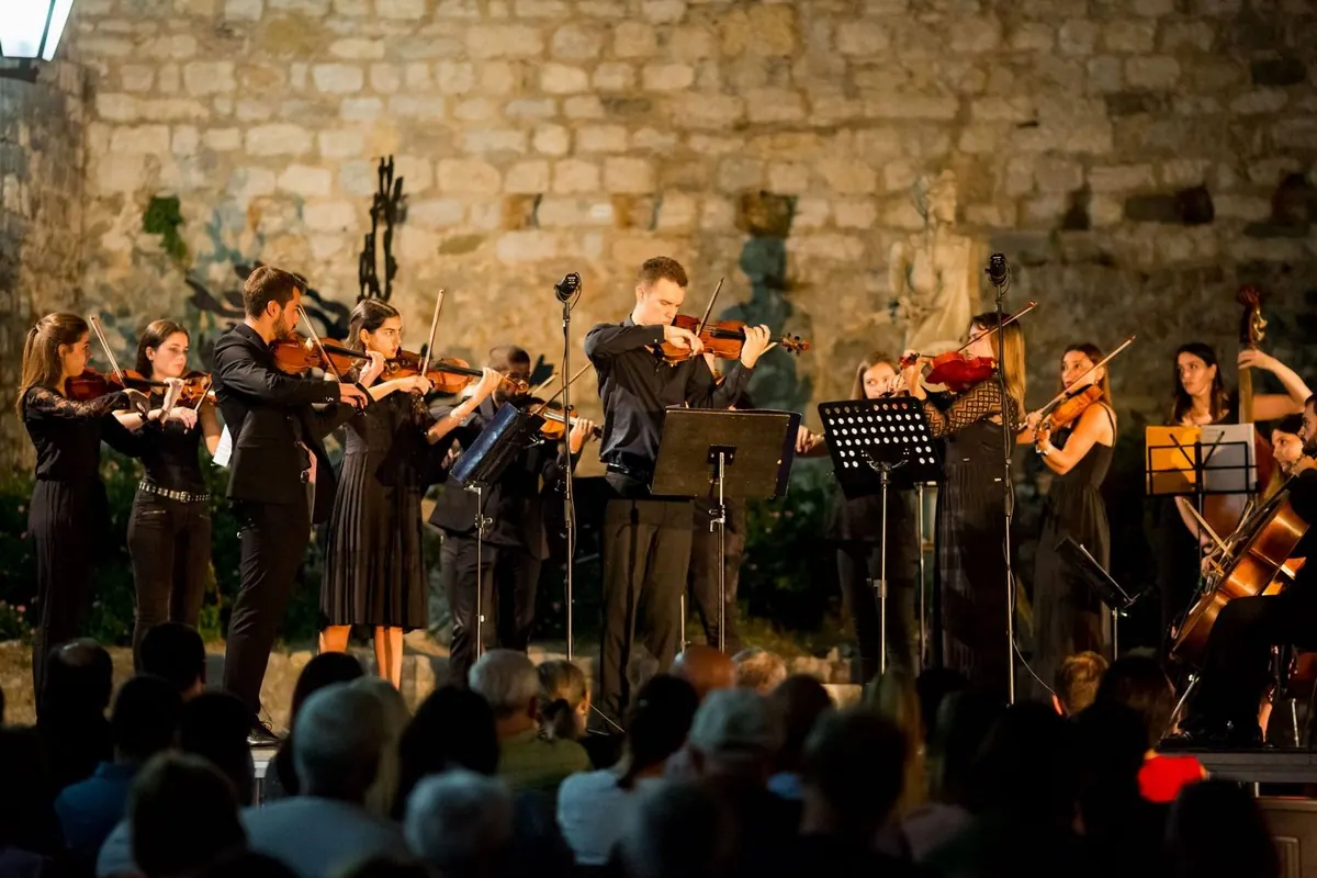 Orkestar svira uz kameni zid Muzeja Starog grada u Ulcinju, publika u prvom planu