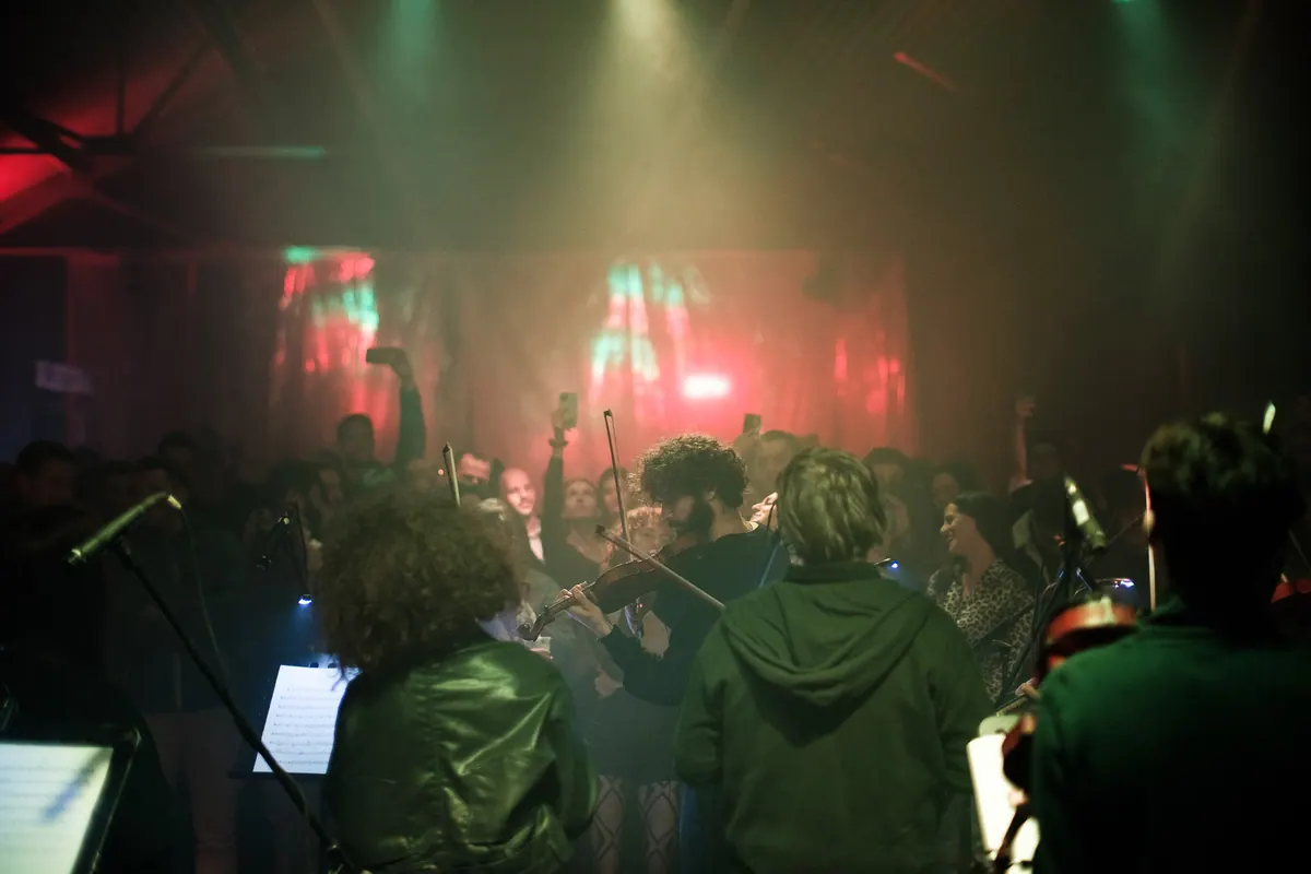 The orchestra’s strings on stage in coloured light, the audience in front