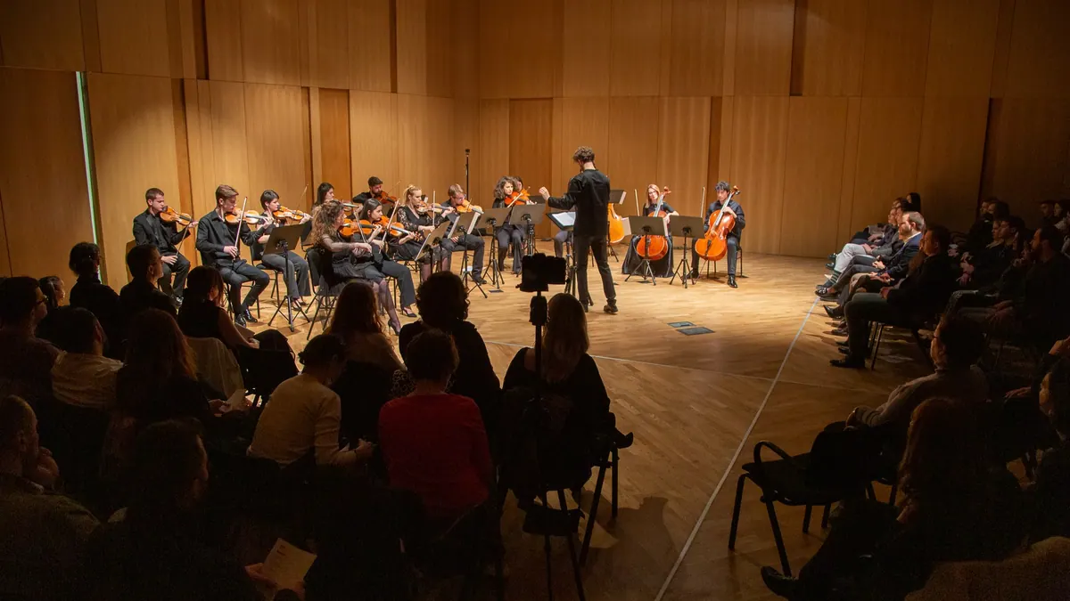 The orchestra playing in a circle in the Chamber Hall of the Music Centre of Montenegro, the audience around it