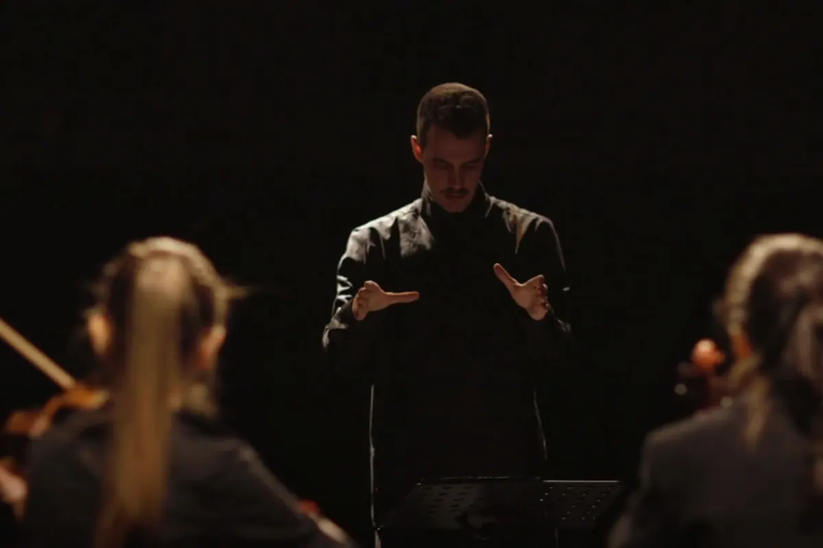 The conductor in black conducting with his hands, musicians blurred in the foreground